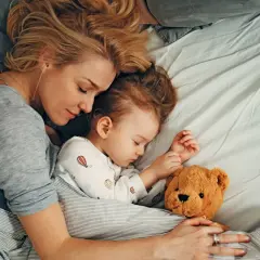 Mutter und Kind schlafen eng umschlungen mit Teddybär. Die beste Schlafzeit für die ganze Familie.