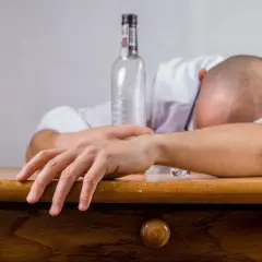Mann schläft betrunken am Tisch, eine leere Flasche neben sich. Alkohol kann Schlafapnoe verschlimmern.
