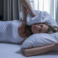 Frau im Bett versucht, Lärm mit Kissen abzuschirmen. Sie sucht verzweifelt nach einem Therapieplatz.