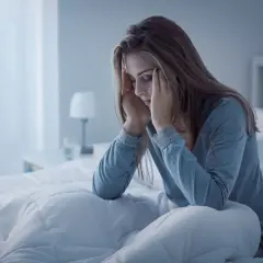 Frau sitzt im Bett, hält sich die Schläfen. Sie fragt sich, was tun wenn man nicht durchschlafen kann.