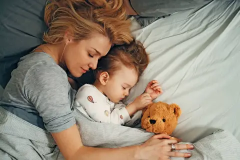 Mutter und Kind schlafen eng umschlungen mit Teddybär. Die beste Schlafzeit für die ganze Familie.