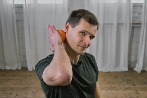 Mann mit Orange am Nacken, zeigt, wie man das Nacken einrenken selber machen kann.