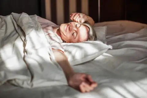 Frau erwacht lächelnd im Bett, genießt die Sonne. Erfüllt die mindest schlafzeit für Wohlbefinden.