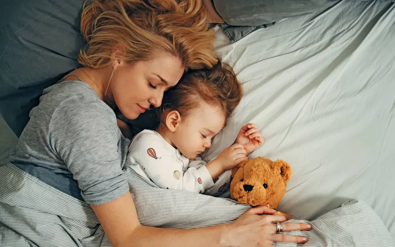 Mutter und Kind schlafen eng umschlungen mit Teddybär. Die beste Schlafzeit für die ganze Familie.