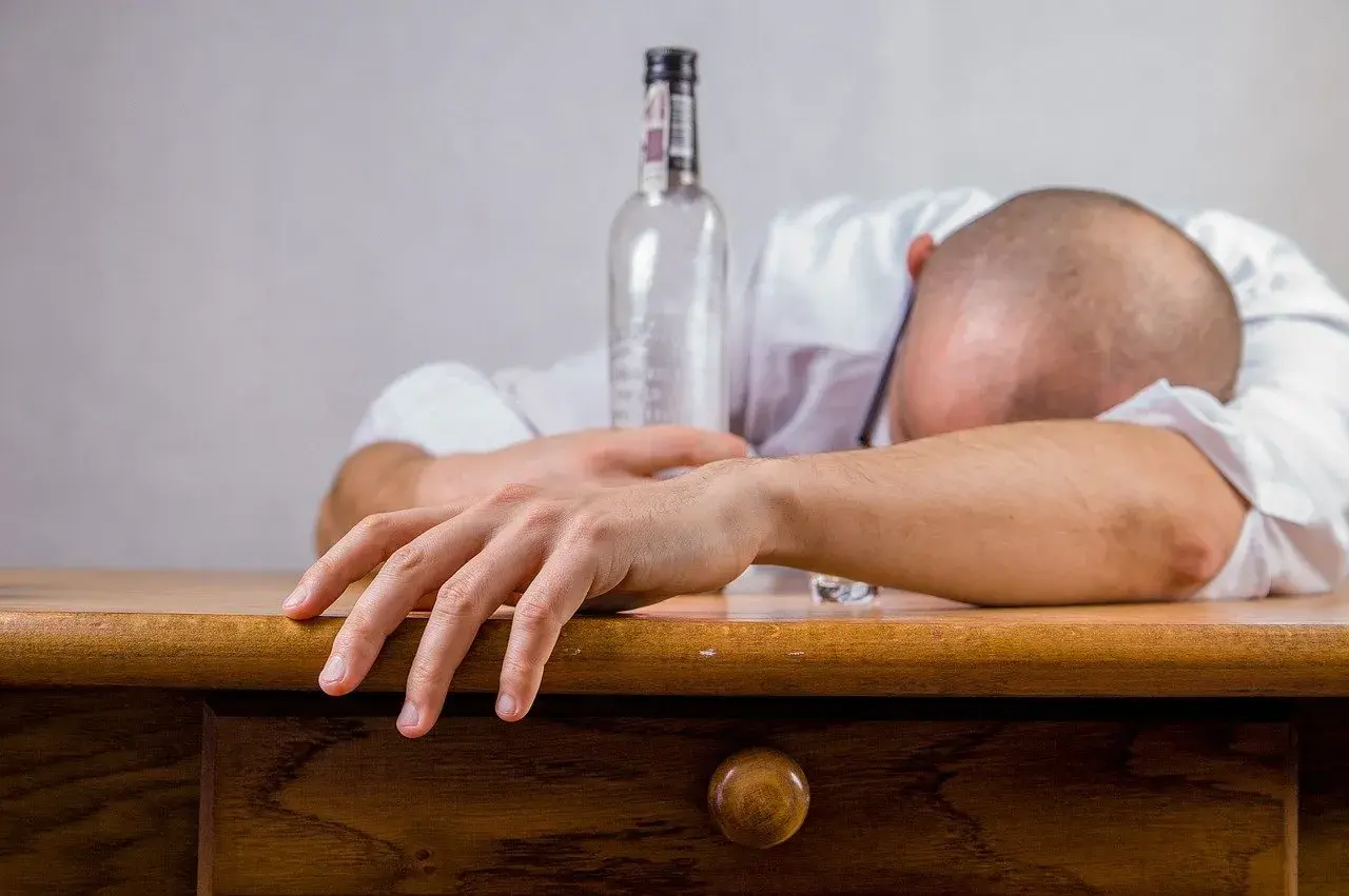 Mann schläft betrunken am Tisch, eine leere Flasche neben sich. Alkohol kann Schlafapnoe verschlimmern.