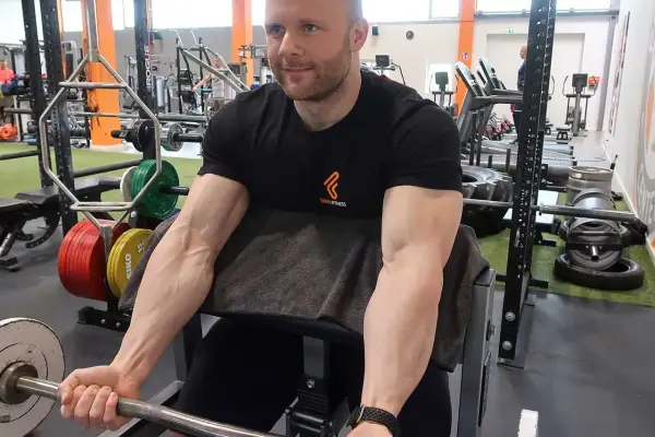 Mann im Fitnessstudio trainiert Bizeps mit Langhantel. Deutlich sichtbare Muskeln beim Bizeps dehnen.
